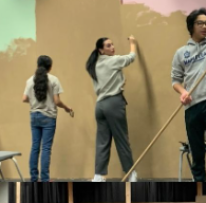 three students paint a set onstage